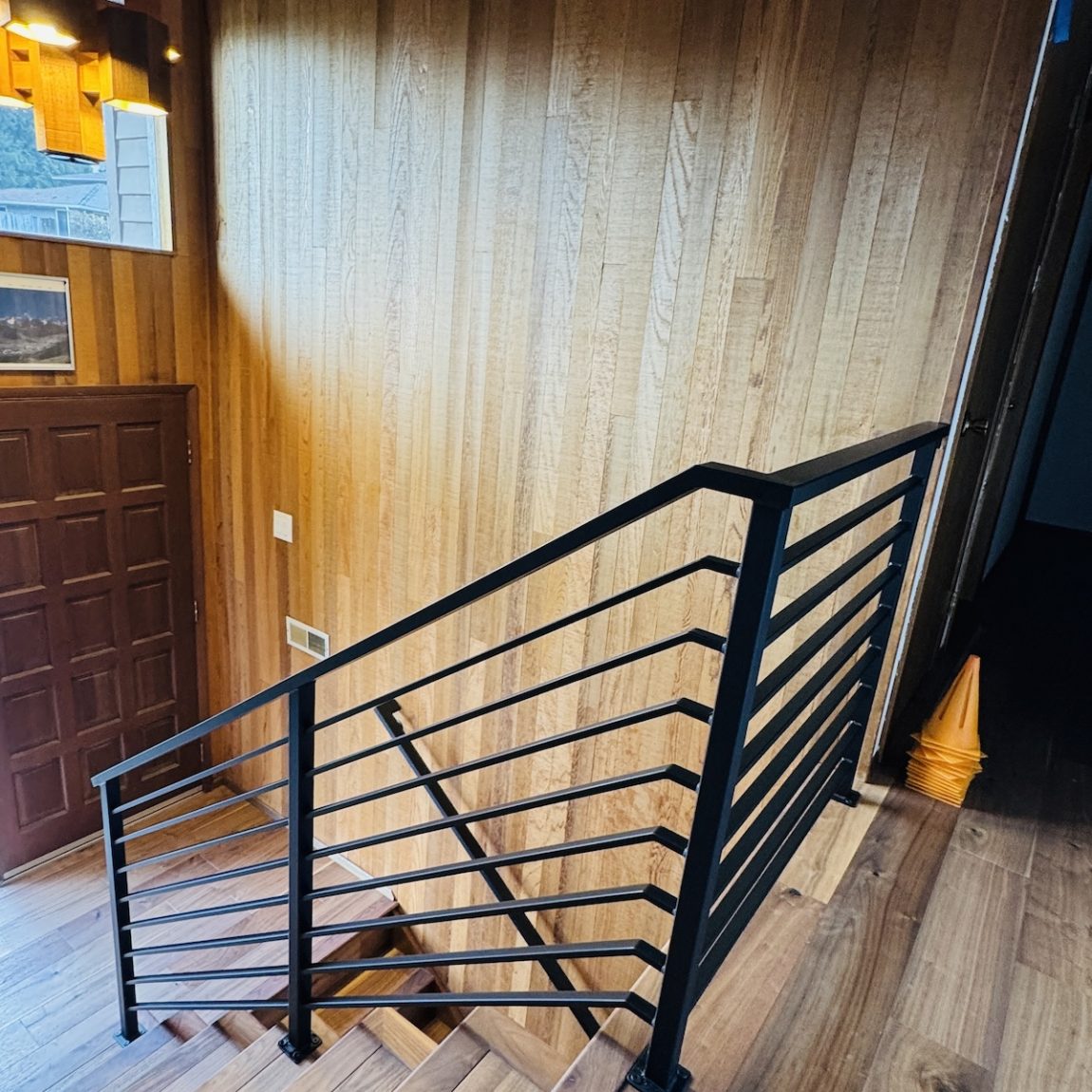 Modern indoor staircase with black horizontal metal railing, carpeted steps, and neutral-colored walls.